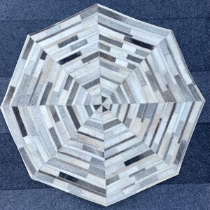Puede incluir: Una alfombra octogonal hecha de piezas de cuero cosidas juntas en un patrón geométrico, con tonos de blanco, gris y marrón.