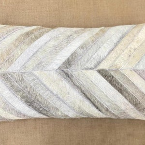 May include: A white and grey chevron patterned throw pillow made of cowhide.