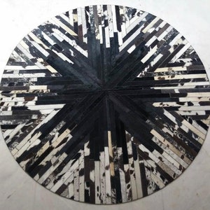 Puede incluir: Una alfombra redonda de piel de vaca negra y blanca con un patrón de estrella. La alfombra está hecha de tiras de cuero cosidas juntas.