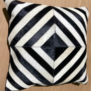 May include: Black and white striped throw pillow with a geometric pattern. The pillow is made of cowhide and has a soft, luxurious feel.