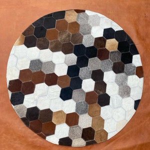 Può includere: Un tappeto rotondo in pelle di mucca multicolore con un motivo a nido d'ape. Il tappeto è realizzato in diverse tonalità di pelle marrone, nero, bianco e grigio.