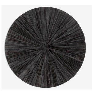 Może przedstawiać: Okrągły, czarny dywan skórzany z wzorem promieni słonecznych. Dywan wykonany jest z pojedynczych kawałków skóry, które są zszyte ze sobą, tworząc wzór promieni słonecznych.