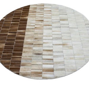 Può includere: Tappeto rotondo in pelle di mucca marrone e bianco con un motivo geometrico. Il tappeto è realizzato con strisce di pelle cucite insieme in un design patchwork.