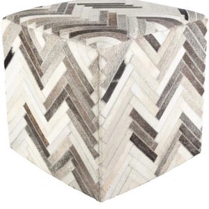 Może przedstawiać: Kwadratowy puf z geometrycznym wzorem w kolorze białym i szarym wykonanym ze skóry. Puf jest wykonany z wielu kawałków skóry zszytych ze sobą, tworząc wzór w jodełkę.