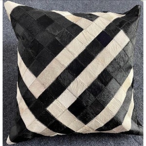 May include: Black and white cowhide pillow with a geometric pattern. The pillow is made of leather and has a soft, luxurious feel.