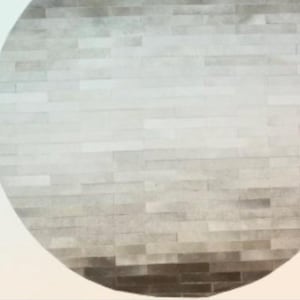 Puede incluir: Primer plano de una pared circular texturizada hecha de azulejos rectangulares de color gris claro y marrón. Los azulejos están dispuestos en un patrón escalonado, creando un sutil efecto degradado.