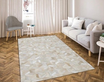May include: A white and beige cowhide rug with a geometric pattern. The rug is laid out on a hardwood floor in a living room setting.
