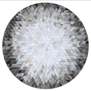 Może przedstawiać: Okrągły dywan z krowiej skóry w kolorze szarym i białym z geometrycznym wzorem. Dywan wykonany jest z wielu małych, diamentowych kawałków skóry.