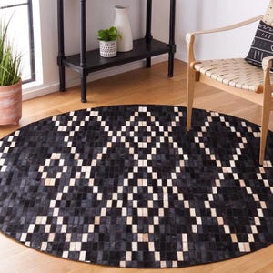 Könnte beinhalten: Schwarz-weißer Kuhfellteppich mit geometrischem Muster. Der Teppich ist rund und hat einen Fransenrand.