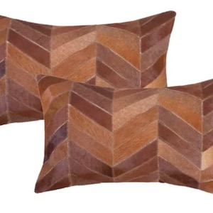 May include: Two brown and beige chevron patterned throw pillows made of cowhide leather.