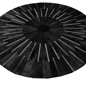 May include: A round rug in black and white with a sunburst design. The rug is made from cowhide and has a distinctive, modern style.