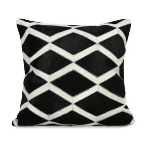 May include: Black and white geometric patterned pillow cover made of cowhide. The pillow cover features a diamond pattern with white stitching.