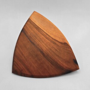 May include: A wooden, triangular cutting board with a natural wood grain pattern. The board has a smooth surface and a warm, brown color. The shape is ideal for serving appetizers or as a decorative kitchen item.