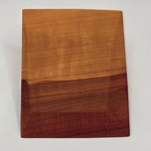 May include: A rectangular wooden cutting board with a two-tone color scheme. The top portion is a light brown, transitioning to a darker reddish-brown at the bottom. The wood grain is visible, adding texture to the surface.