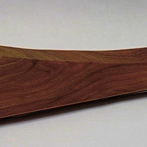 May include: A wooden, curved tray with a rich, dark brown wood grain. The tray has a triangular shape on one end and a curved, boat-like design. The wood grain is visible across the surface, highlighting the natural patterns and textures of the material.