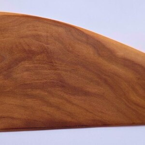 May include: A wooden cutting board with a teardrop shape. The board is made of light and dark brown wood, with visible grain patterns. The board is approximately 18 inches long and 8 inches wide.
