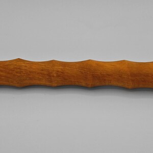 Puede incluir: Un rodillo de madera con acabado natural. El rodillo es de color marrón claro y tiene un diseño acanalado a lo largo del cuerpo principal. Los extremos son lisos y redondeados. El rodillo está diseñado para su uso en repostería y cocina.