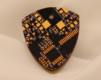 Könnte beinhalten: Ein Gitarrenplektrum mit einem schwarzen Leiterplatten-Design und gelben Akzenten. Das Plektrum hat eine abgerundete Dreiecksform mit einem kleinen Loch oben. Das Design umfasst verschiedene elektronische Komponenten und Beschriftungen.