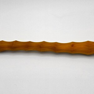 Puede incluir: Un rodillo de madera con un acabado marrón claro natural. El rodillo tiene un diseño acanalado a lo largo de su longitud, con mangos lisos y redondeados. La veta de la madera es visible.