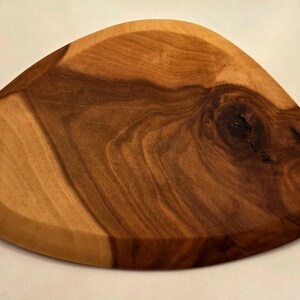 May include: A wooden serving tray with a unique, organic shape. The tray is crafted from a light and dark brown wood, showcasing the natural grain and a prominent knot. The edges are slightly raised, creating a subtle border.