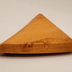 May include: A triangular wooden piece with a smooth, light brown surface. The wood has a natural grain pattern and a slightly curved edge.