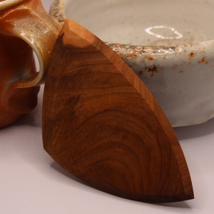 May include: A dark brown wooden utensil shaped like a triangle with rounded edges. The utensil is made of wood with a natural grain pattern.