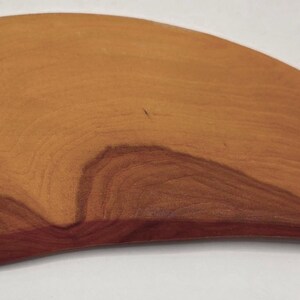 May include: A wooden, teardrop-shaped cutting board with a natural wood grain pattern. The board has a smooth, polished surface and a rich, reddish-brown color. The board is approximately 12 inches long.