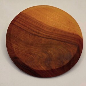 May include: A round wooden plate with a rich, warm brown color and a darker, reddish-brown rim. The wood grain is visible, adding texture to the surface. The plate is likely for serving or display.
