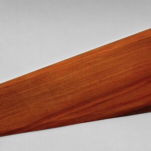 May include: A wooden fan blade with a curved end and a pointed tip. The blade is a warm reddish-brown color, with visible wood grain. The design is sleek and modern, suitable for home decor.