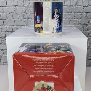 May include: A ceramic mug featuring Toy Story characters including Bo Peep and a blue-helmeted figure, paired with a red cardboard box. The box base displays The Disney Store text, manufacturing details, and price labels of $7.00 US and $10.00 CDN.