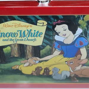 May include: A red metal lunchbox featuring a colorful illustration from Walt Disney's "Snow White and the Seven Dwarfs." The image shows Snow White with forest animals. The lunchbox has a silver clasp.