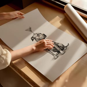 May include: A black and white illustration of a dog with a martini glass balanced on its head. The dog is lying down, and the artwork is on a large sheet of paper. The paper is being held by a person.
