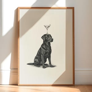 May include: A framed print featuring a black Labrador Retriever with a martini glass balanced on its head. The dog is depicted in a seated position, with a detailed pencil-style drawing. The artwork is set against a neutral background.