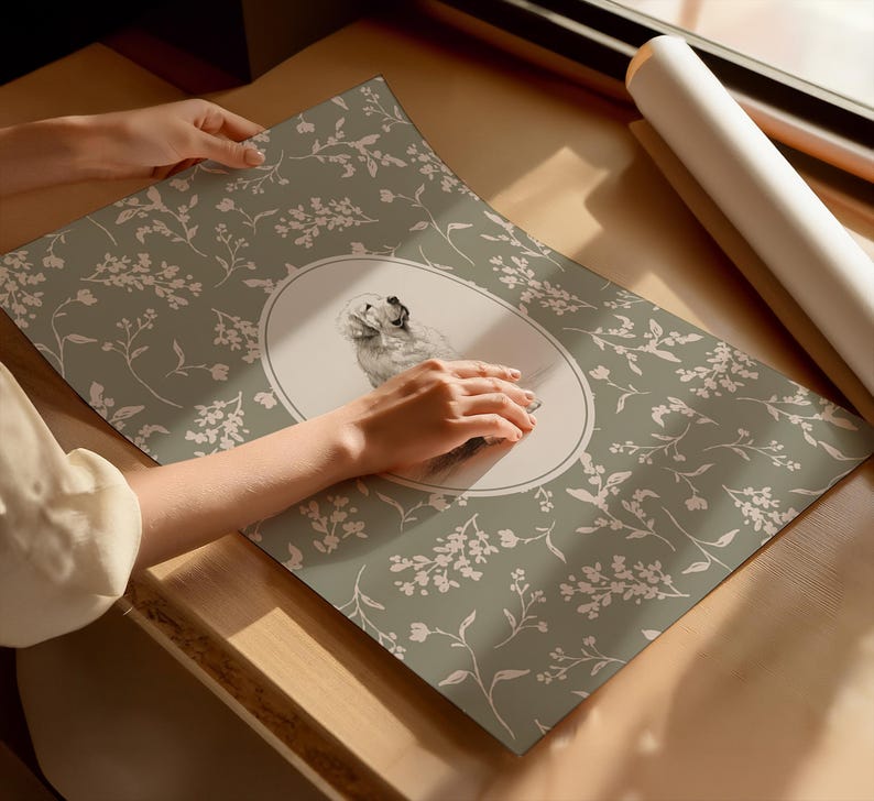May include: A poster with a dog illustration in an oval frame, set against a sage green backdrop with a white floral design. The poster is displayed on a wooden surface. The overall aesthetic is delicate and artistic.