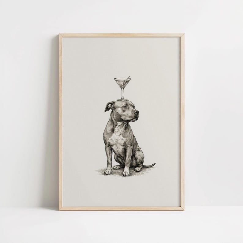 May include: A framed black and white print of a seated dog with a martini glass balanced on its head. The martini glass contains a green olive. The dog is a pit bull terrier, and the print has a light beige background.