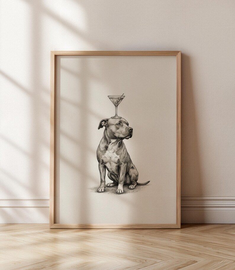 May include: A framed print featuring a detailed pencil drawing of a seated dog with a martini glass balanced on its head. The artwork is in grayscale, with a light beige background and a natural wood frame. The dog is a pit bull type breed.