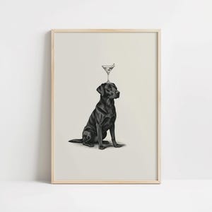 May include: A framed print featuring a black Labrador Retriever sitting upright with a martini glass balanced on its head. The artwork is a black and white illustration with a light background and a wooden frame.