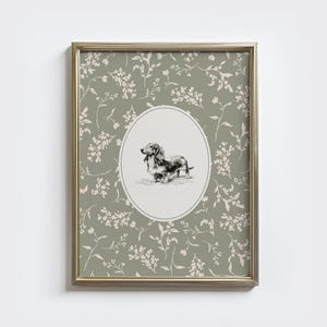 May include: A framed print with a gold-toned frame. The print features a black and white drawing of a dachshund dog in an oval frame. The background is sage green with a floral pattern. The overall aesthetic is vintage.