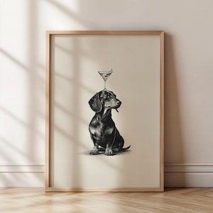 May include: Framed art print in black and white, depicting a dachshund with a martini glass balanced on its head. The dog is illustrated in detail, sitting upright. The martini glass contains an olive. The artwork is presented in a wooden frame.