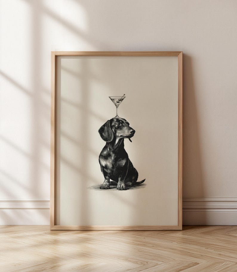May include: Framed art print in black and white, depicting a dachshund with a martini glass balanced on its head. The dog is illustrated in detail, sitting upright. The martini glass contains an olive. The artwork is presented in a wooden frame.