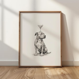 May include: A framed black and white print featuring a seated dog with a martini glass balanced on its head. The artwork is set against a neutral background, with a wooden frame. The print is displayed on a wooden floor.