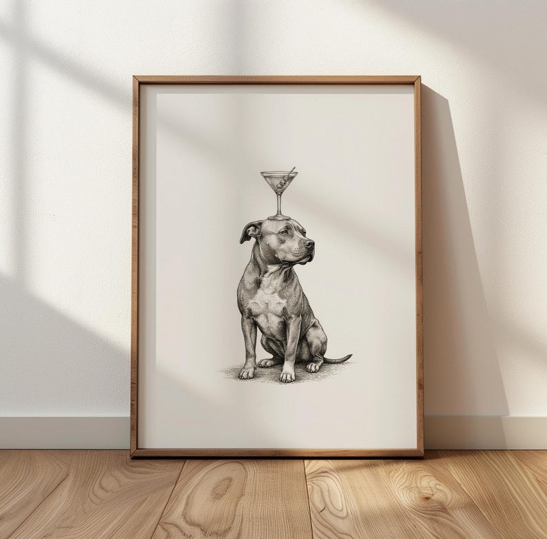 May include: A framed black and white print featuring a seated dog with a martini glass balanced on its head. The artwork is set against a neutral background, with a wooden frame. The print is displayed on a wooden floor.