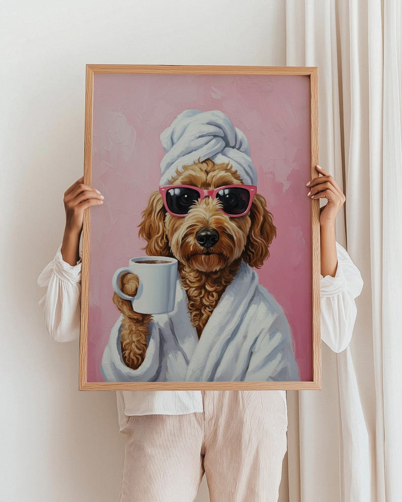 以下が含まれることがあります： サングラス、タオル、白いバスローブを着てコーヒーカップを持った犬の額装プリント。犬は茶色で、背景はピンク色です。フレームはライトブラウンです。