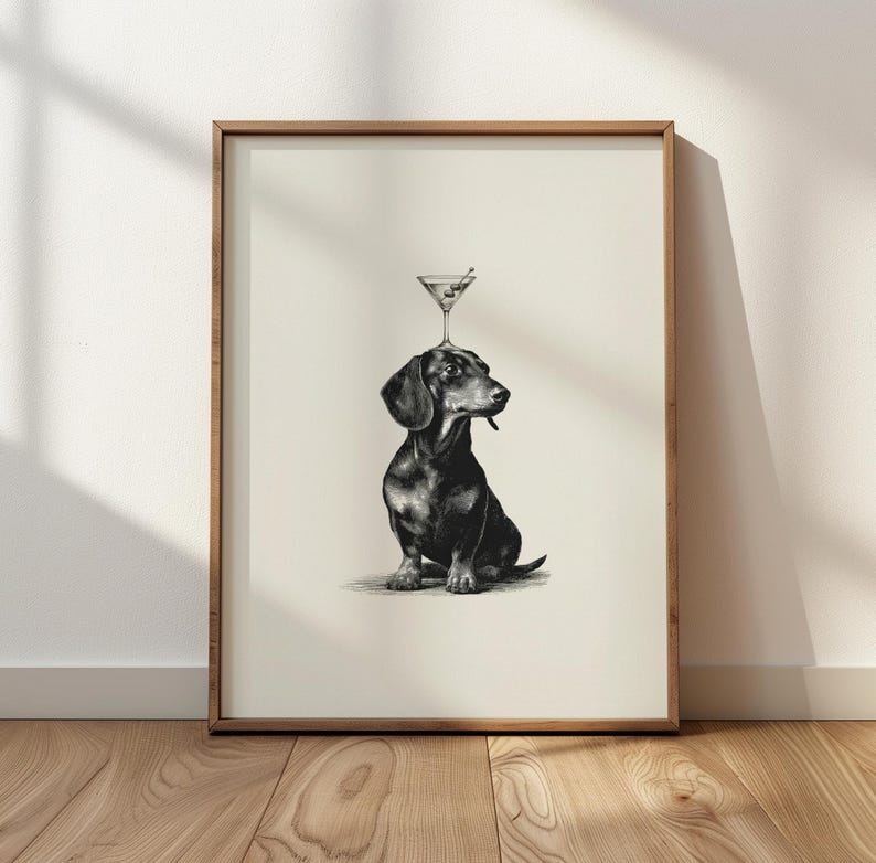 May include: Monochrome art print featuring a dachshund dog with a martini glass balanced on its head. The dog is sitting, with a martini olive in its mouth. The print is in a wooden frame.