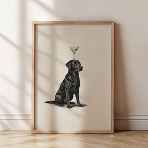 May include: A framed print featuring a black Labrador Retriever with a martini glass balanced on its head. The dog is sitting upright, and the martini glass has an olive. The artwork is in black and white.