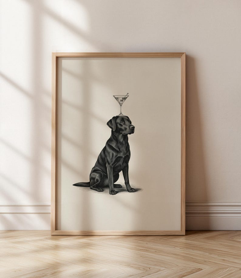 May include: A framed print featuring a black Labrador Retriever with a martini glass balanced on its head. The dog is sitting upright, and the martini glass has an olive. The artwork is in black and white.