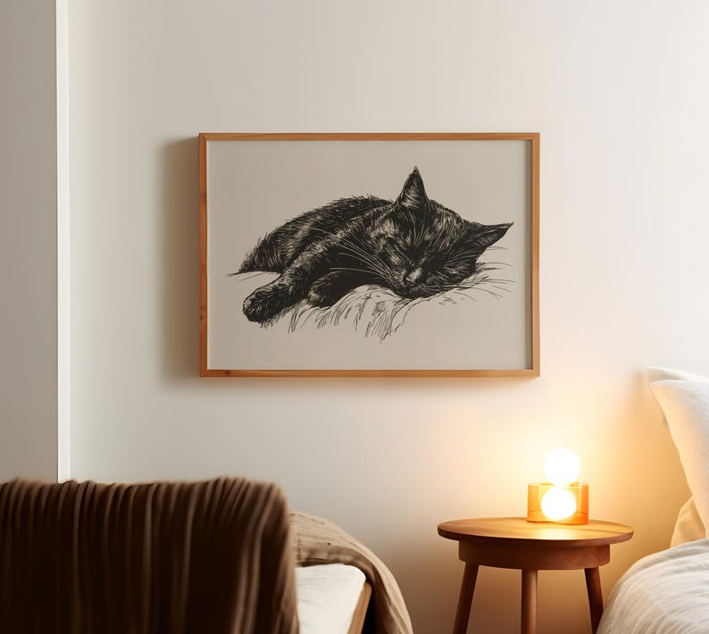 May include: A black and white illustration of a cat sleeping on a pillow, framed in a light wood frame.