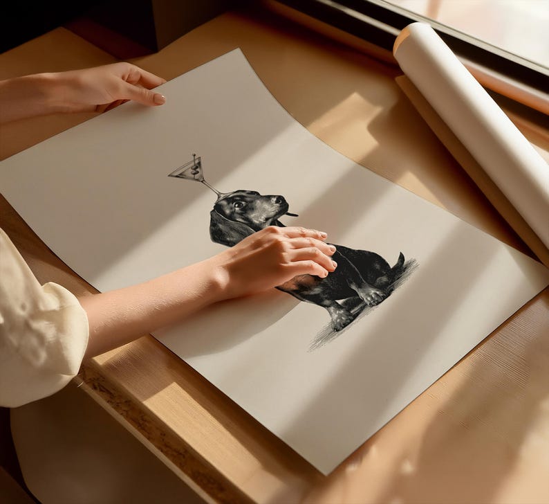 May include: Monochrome art print featuring a dachshund dog with a martini glass balanced on its head. The dog is depicted in a detailed pencil sketch style. The print is on a light beige paper.