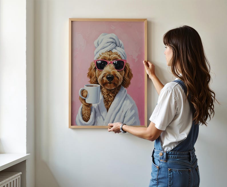 以下が含まれることがあります： サングラス、タオル、バスローブ姿の犬がマグカップを持っているフレーム入りプリント。犬はピンク色の背景に描かれています。フレームは明るい茶色です。