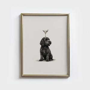 Pode incluir: Uma impressão emoldurada apresenta um cão preto com um copo de martini equilibrado na cabeça. O cão está sentado e o copo de martini tem uma azeitona. A obra de arte é em preto e branco.